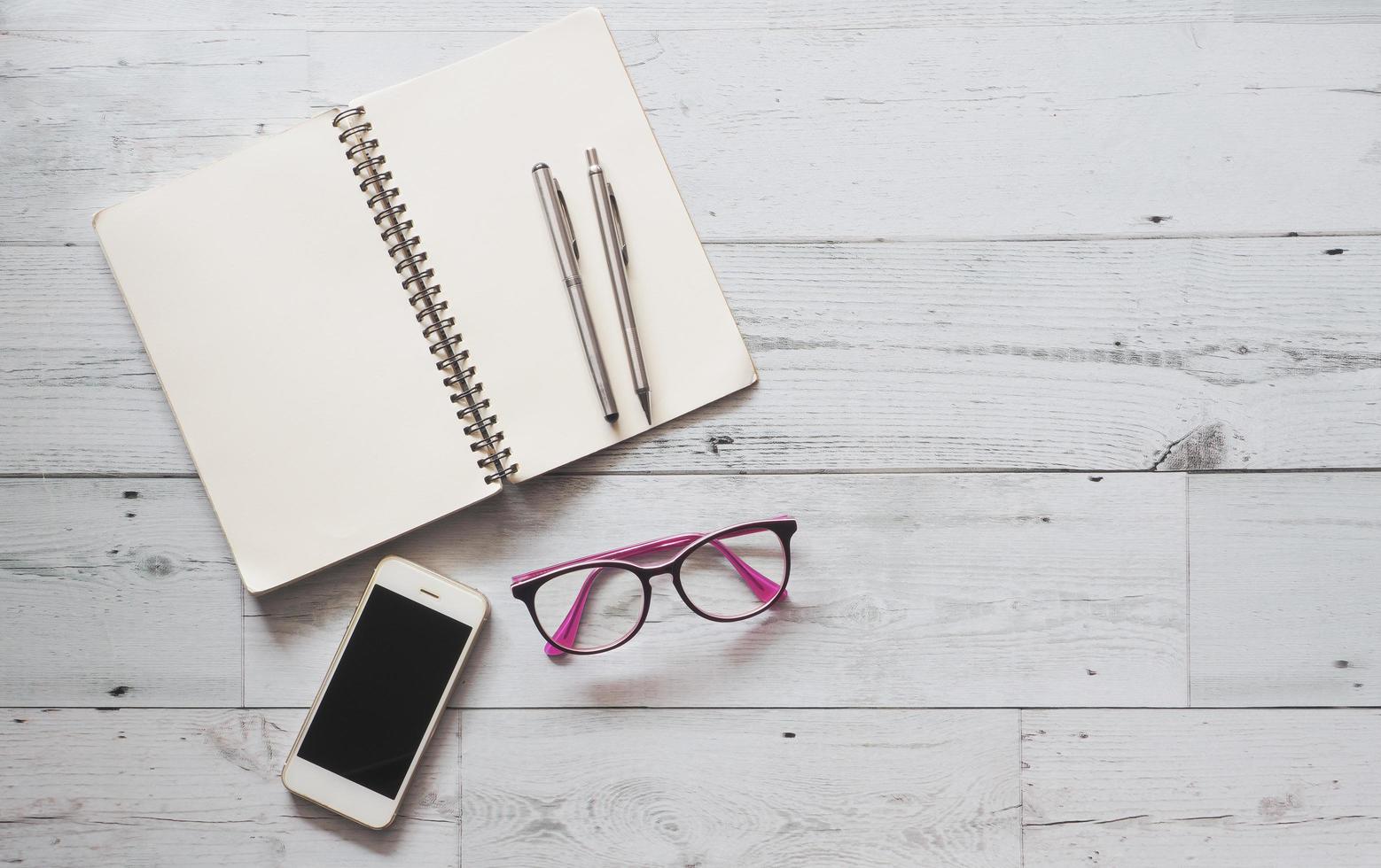 dos bolígrafos plateados en la página en blanco cuaderno abierto con teléfono inteligente y gafas en la mesa de madera blanca sombra natural y espacio de copia de vista superior clara, concepto de negocio foto