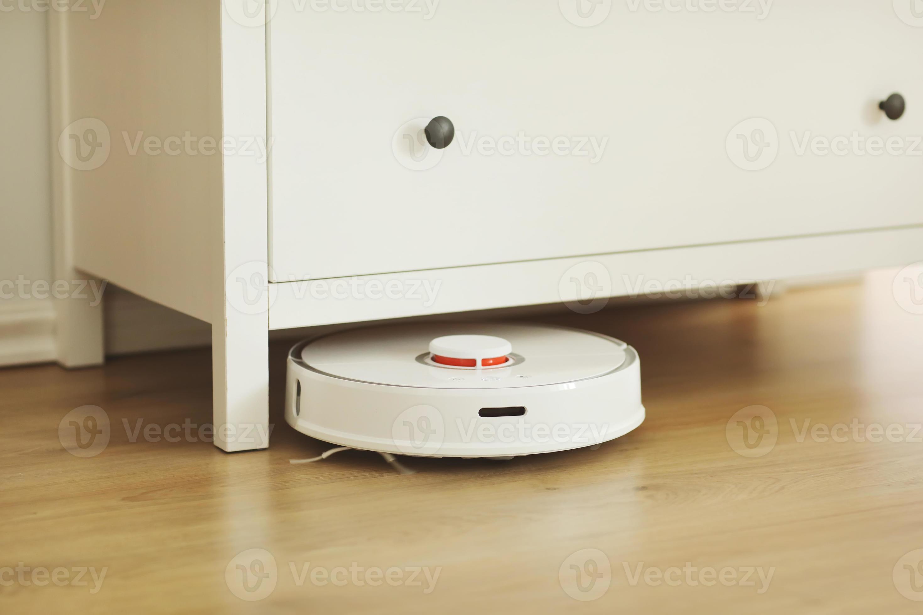 White robotic vacuum cleaner on laminate floor cleaning dust in living