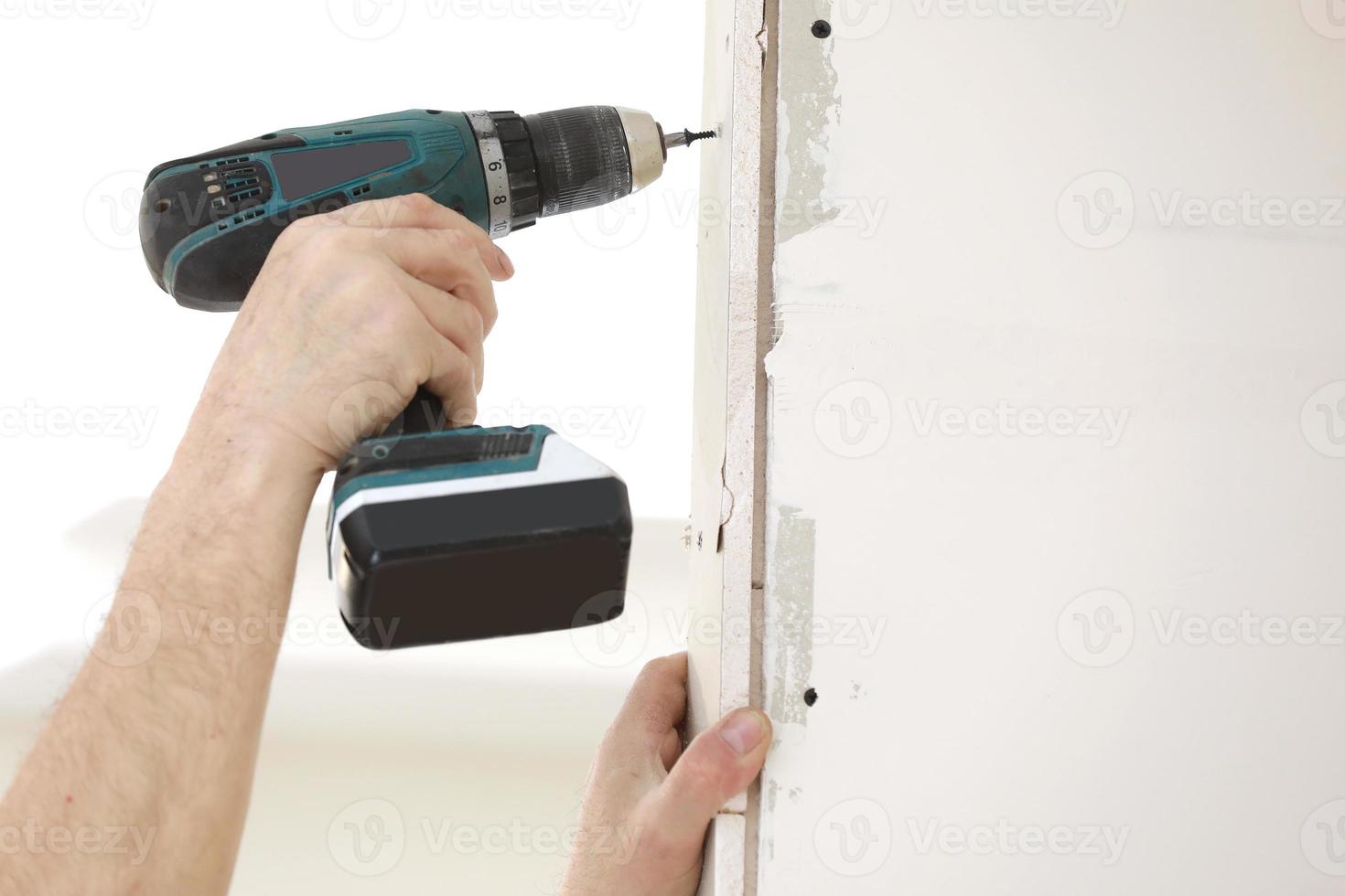 The installer worker in safe medical mask and overalls fixes a detail of the stiffener element with screws using an electric screwdriver to the wall of the metal structure photo
