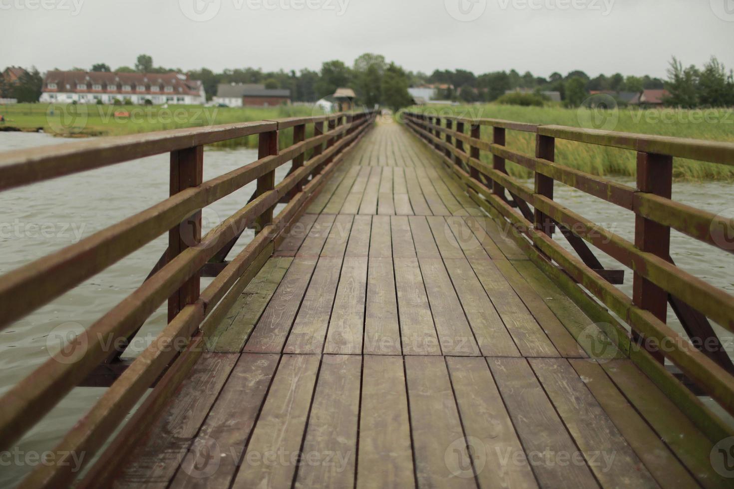 long wooden pedestrian bridge with railings across the river. background of village, srlective focus photo