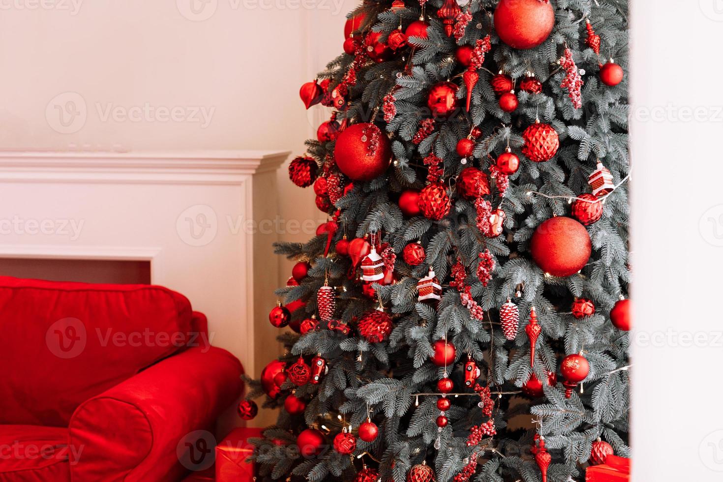 elegantes adornos navideños en el árbol, hermosos juguetes, bolas en colores rojos. gran lazo rojo en la parte superior. ambiente acogedor de navidad en la sala de estar, año nuevo. diseño de interiores festivo. felices vacaciones en casa foto