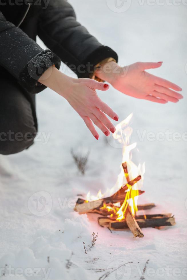 foto recortada de mujer joven calienta sus manos sobre la hoguera en el bosque de invierno. de cerca