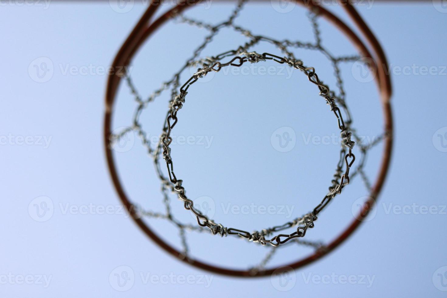 basketball hoop with metal net and wooden backboard on blue sky background. Basketball court outdoors. Recreational sport equipment on streetball field alfresco, playground on street. bottom view photo