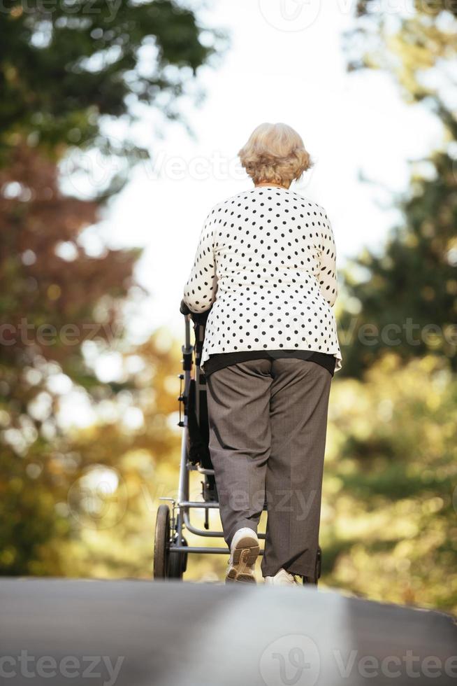 Happy senior lady pushing wheel chair and children. Grandmother and kids enjoying a walk in the park. Child supporting disabled grandparent. Family visit. Generations love and relationship photo