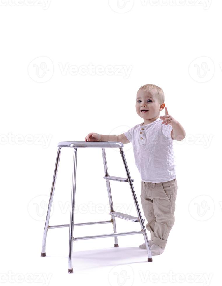 Little boy climbs onto a ladder chair. The beginning of a career concept. Funny little boy isolated on white background. photo