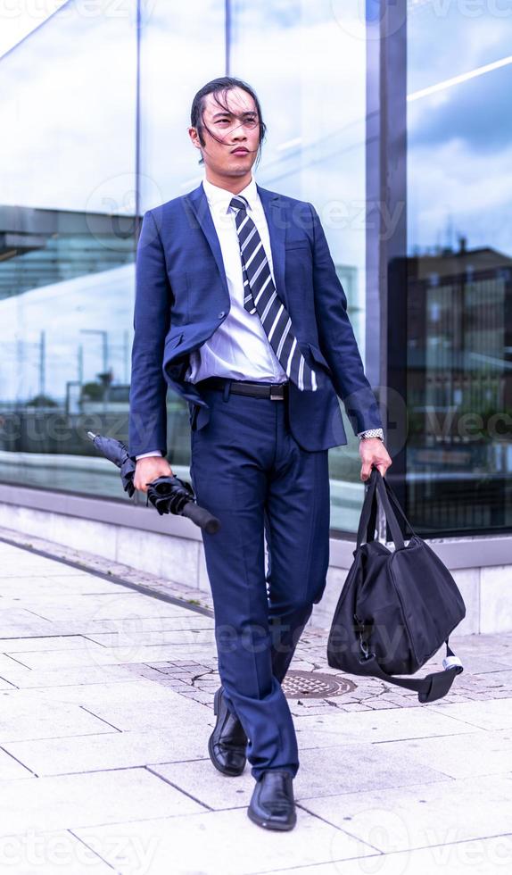 apuesto hombre de negocios asiático con traje y caminando al aire libre, gerente exitoso durante el descanso caminando por la ciudad. foto