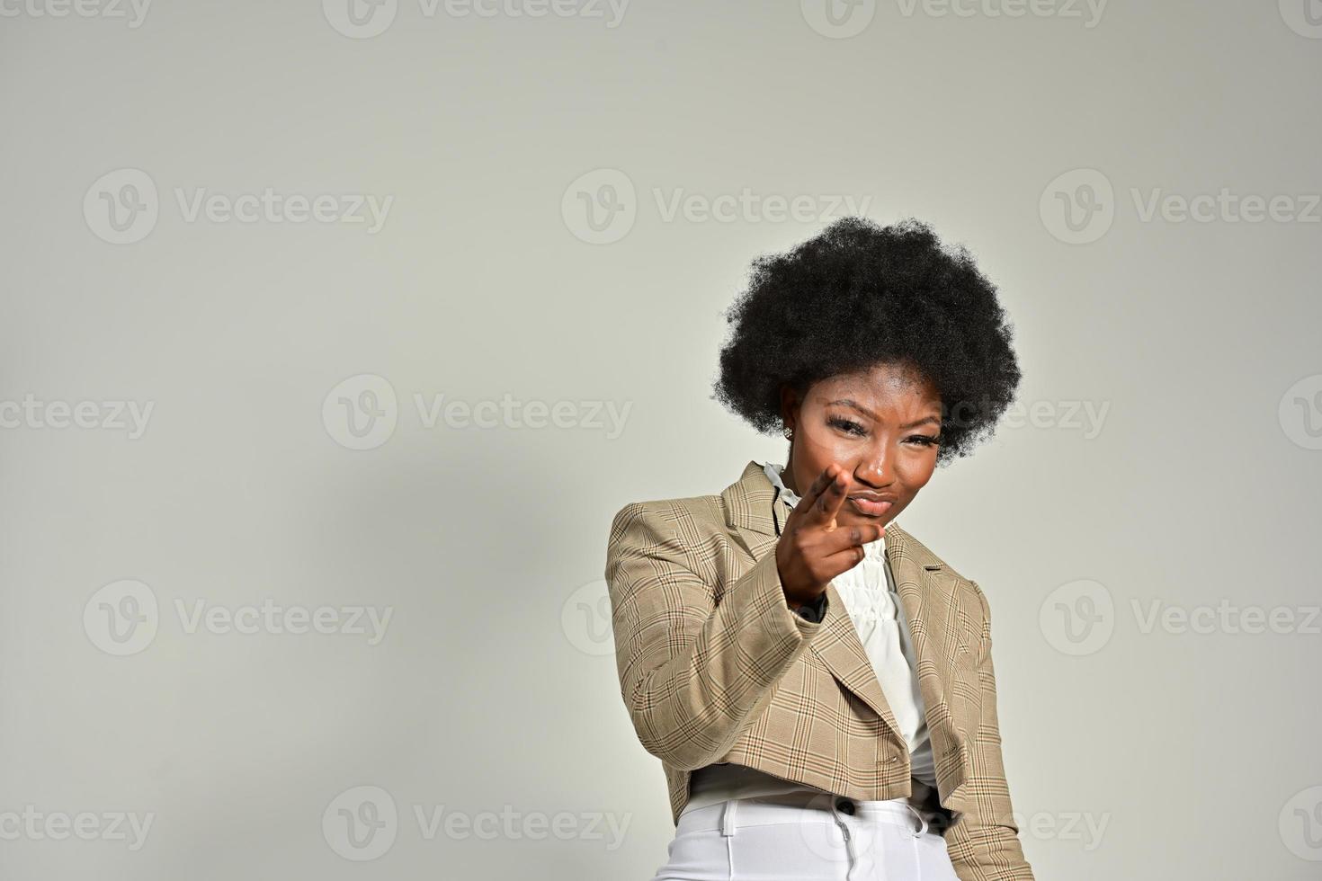 Pretty African American female with trendy accessories and Afro hairstyle looking at camera against gray background photo