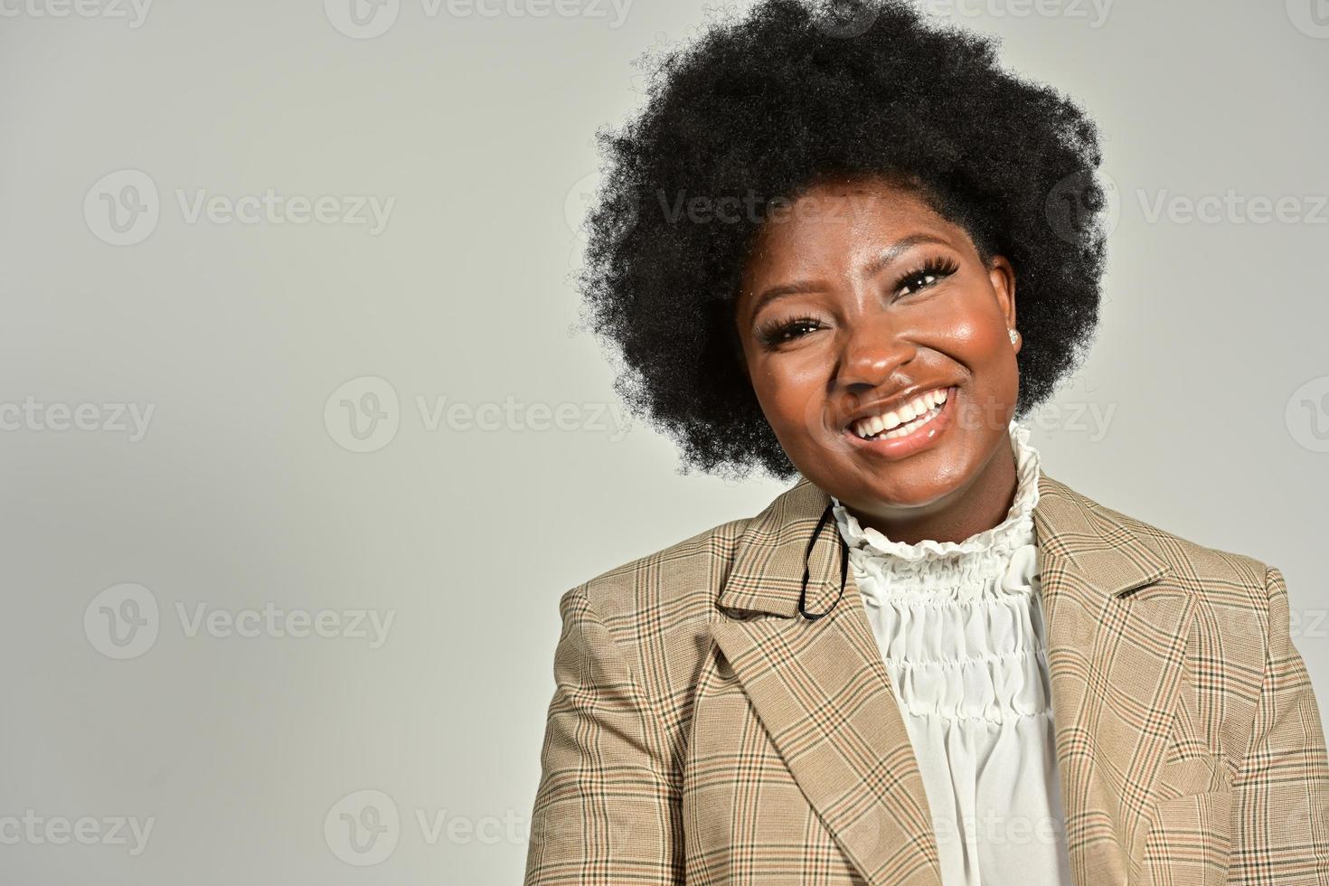 Pretty African American female with trendy accessories and Afro hairstyle looking at camera against gray background photo