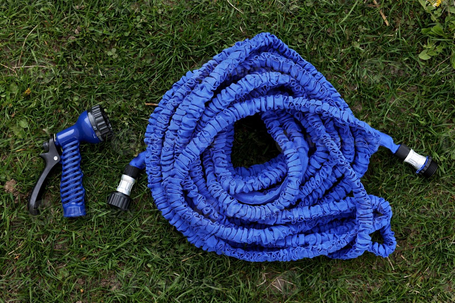 close up of watering hose lies on the grassy ground. blue rubber tube with device for spraying and watering plants in the garden. selective focus. photo