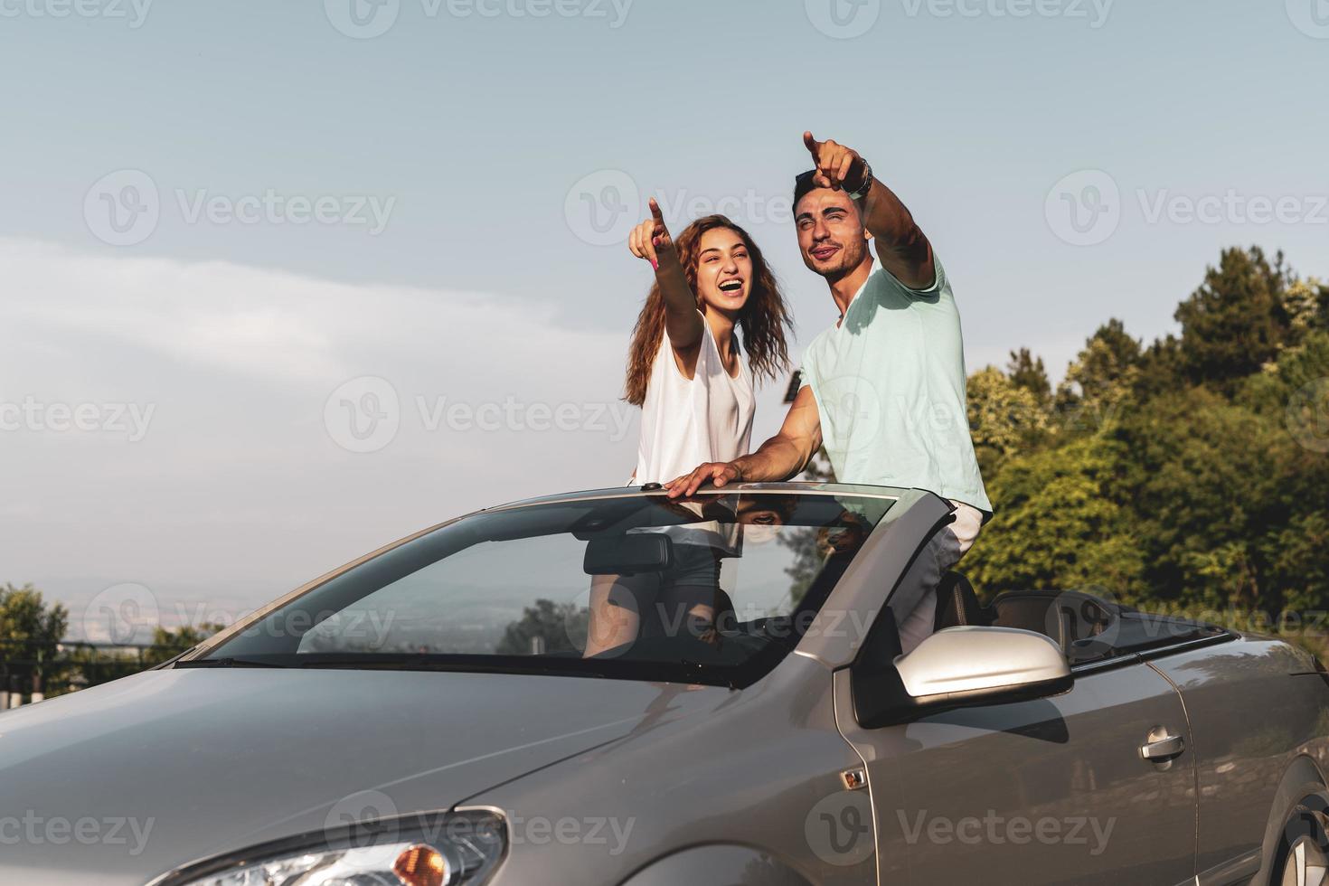 Friends having fun at car trip around the world. Couple in love with arms up on a convertible car. photo