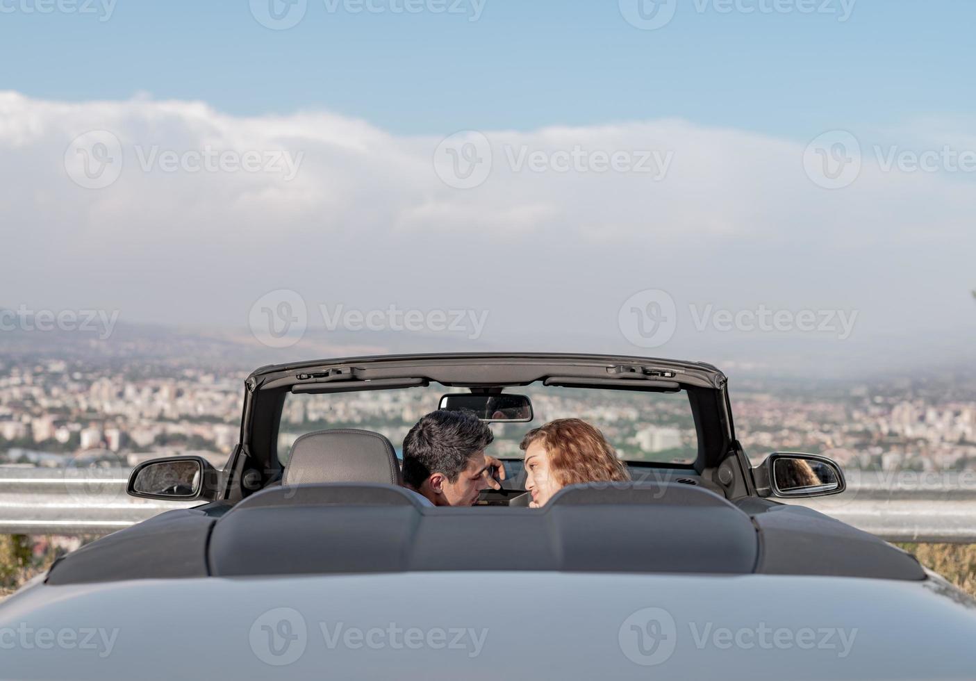 Friends having fun at car trip around the world. Couple in love with arms up on a convertible car. photo