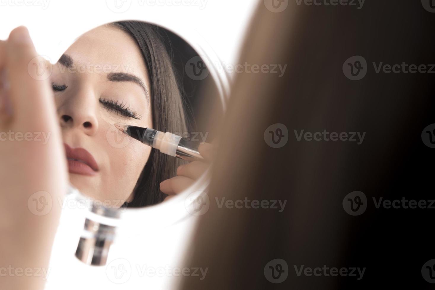 Portrait of a young woman applying liquid make up on her face. Isolated on white background photo