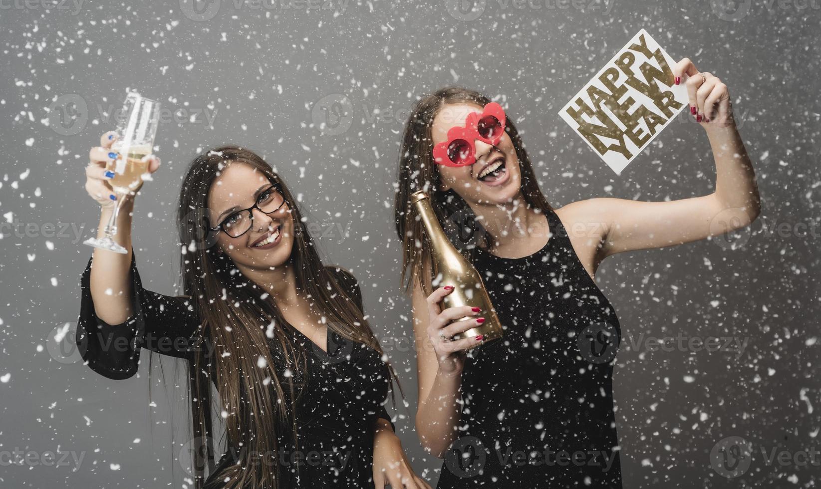 Two female friends celebrating New Year with confetti and champagne holding sign. isolated photo