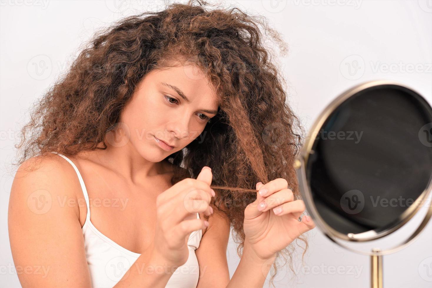 modelo femenino positivo sonriendo para la cámara y tocando el cabello rizado limpio después de la rutina higiénica foto