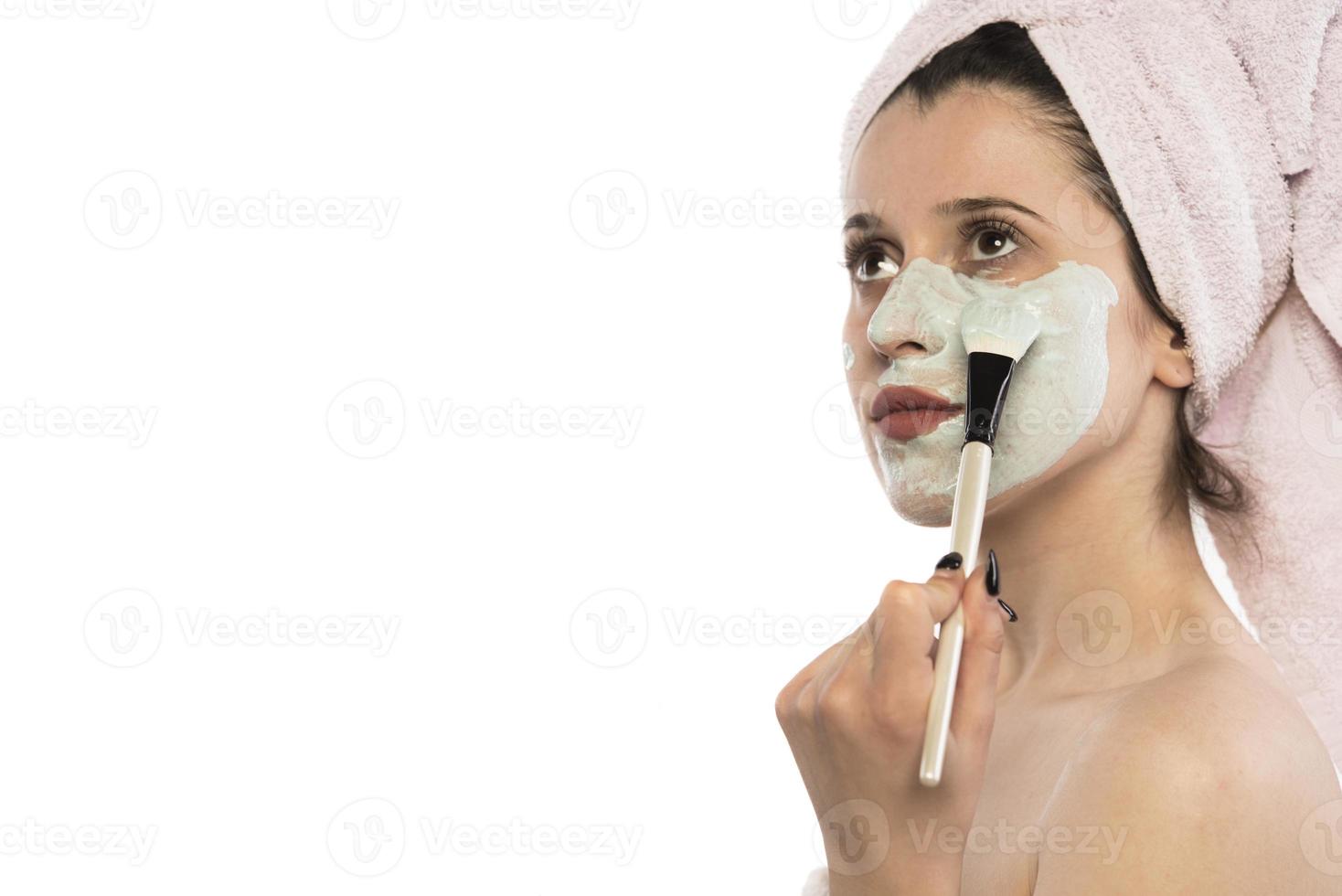Beautiful woman having clay facial mask apply by beautician. photo