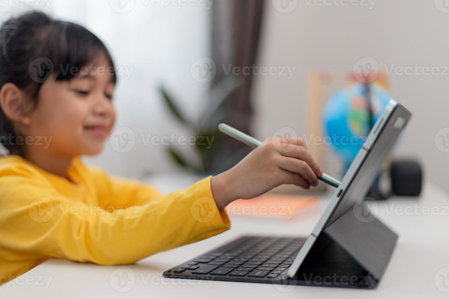colegiala asiática haciendo su tarea con tableta digital en casa. los niños usan aparatos para estudiar. educación y aprendizaje a distancia para niños. educación en el hogar durante la cuarentena. Quédate en casa foto
