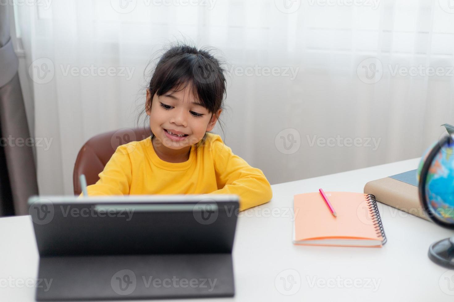 Asian schoolgirl doing her homework with digital tablet at home. Children use gadgets to study. Education and distance learning for kids. Homeschooling during quarantine. Stay at home photo