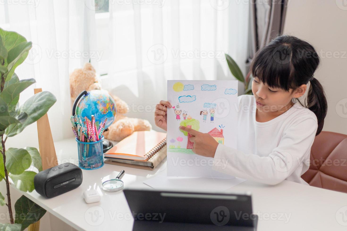 Asian schoolgirl doing her homework with digital tablet at home. Children use gadgets to study. Education and distance learning for kids. Homeschooling during quarantine. Stay at home photo