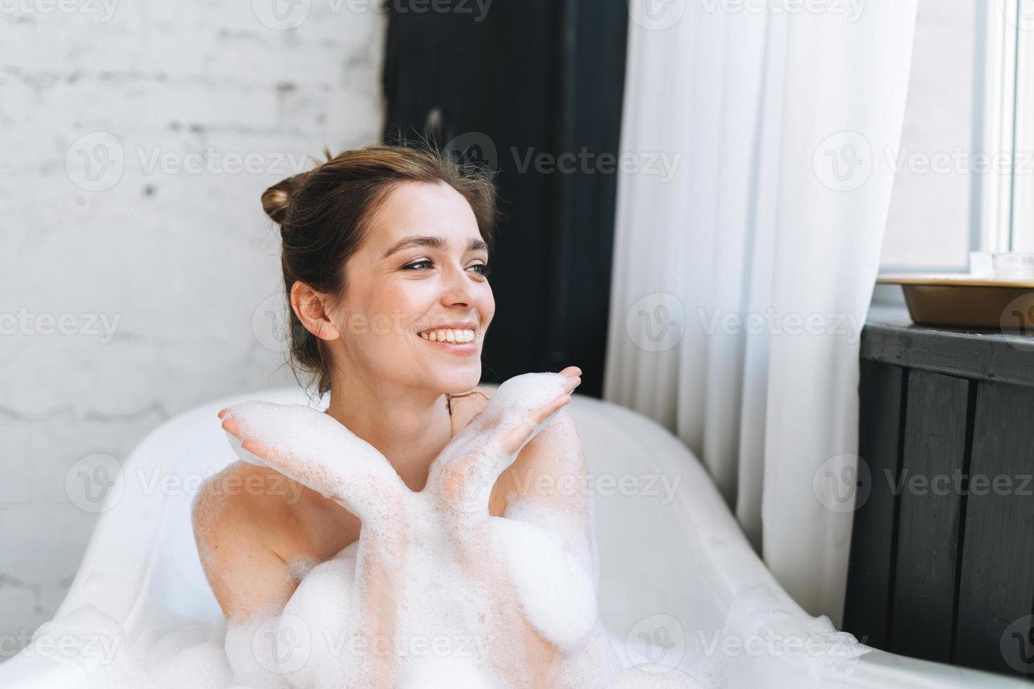 Young happy woman taking bath with foam at home, treat yourself photo