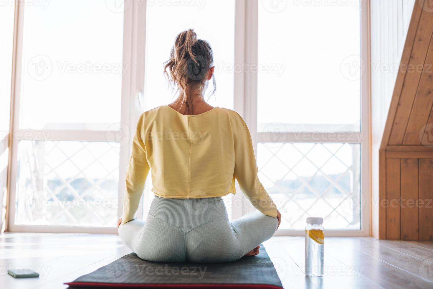 Young sllim fitness blonde woman practice morning yoga near window of home photo
