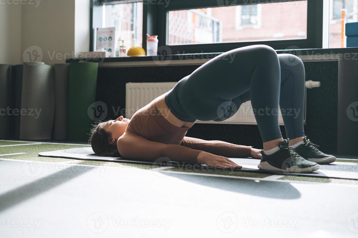 joven morena haciendo pilates de estiramiento, practica yoga en la alfombra en el gimnasio foto