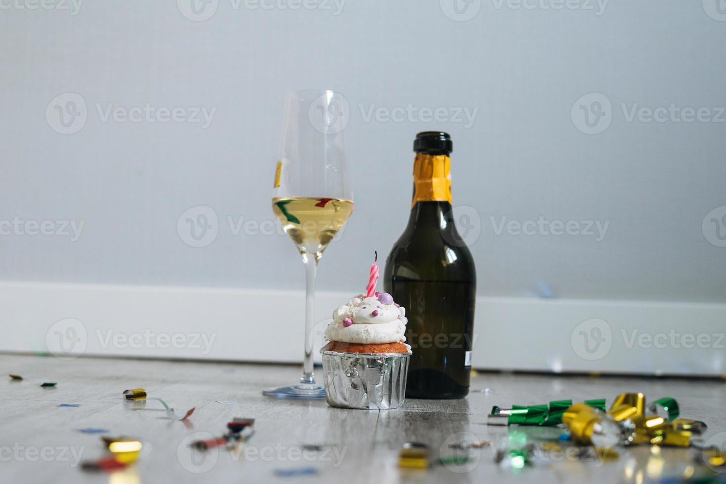 botella y copa de champán y bizcocho con velas en el suelo con confeti después de la fiesta de cumpleaños en casa foto