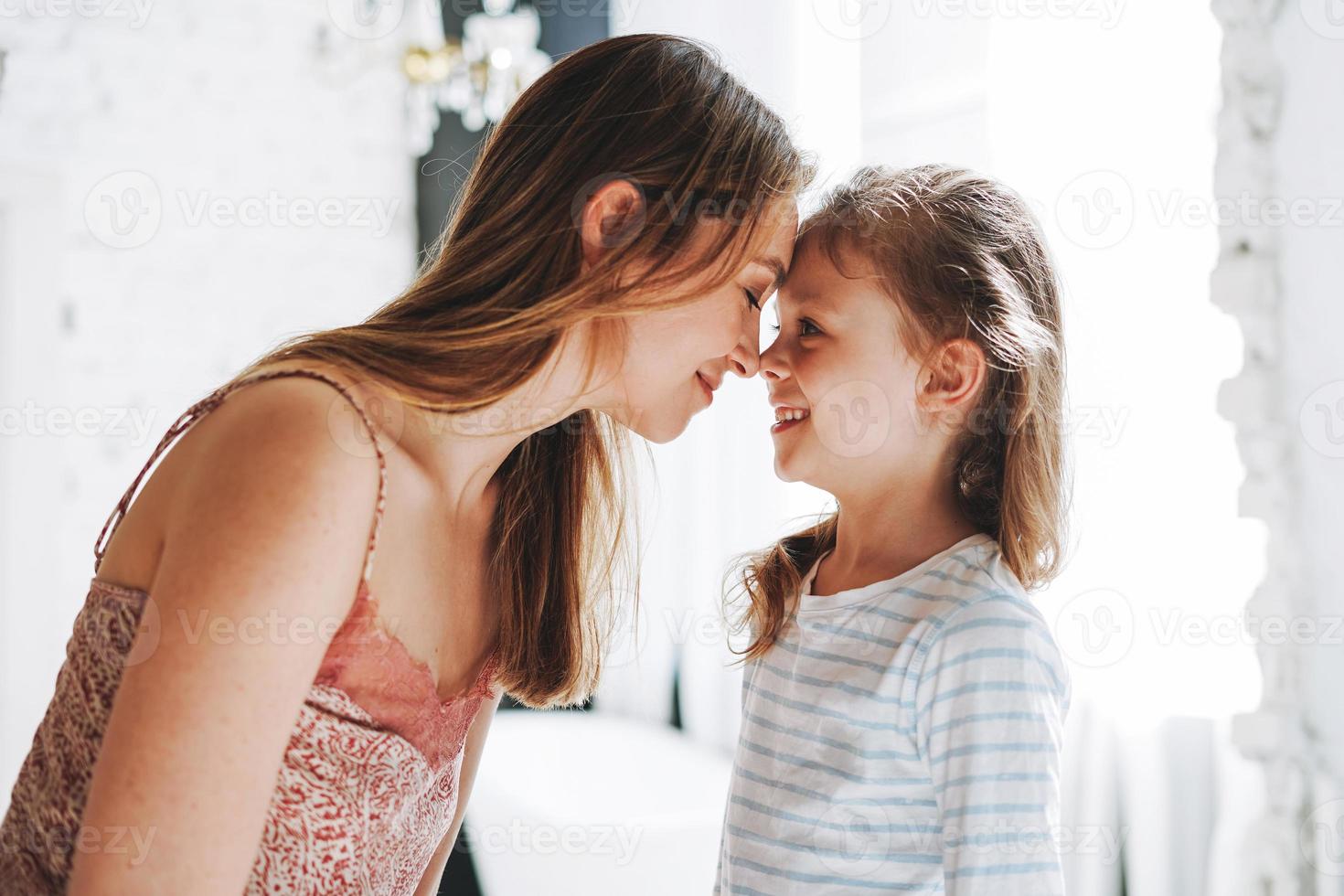 Young mother woman with long hair with little tween girl daughter in pajamas having fun in the morning at home photo