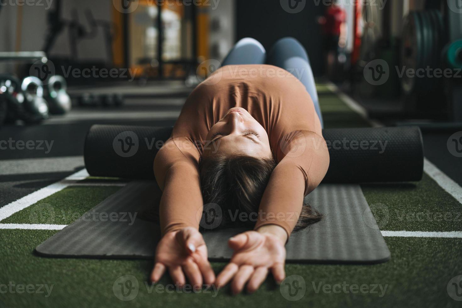 joven morena haciendo pilates de estiramiento en rollo de masaje en el gimnasio del club de fitness foto