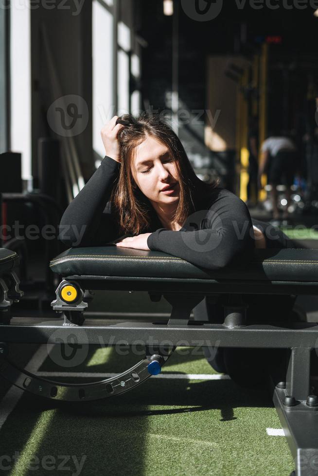 Tired Young fitness brunette woman training on muscles equipment at gym photo