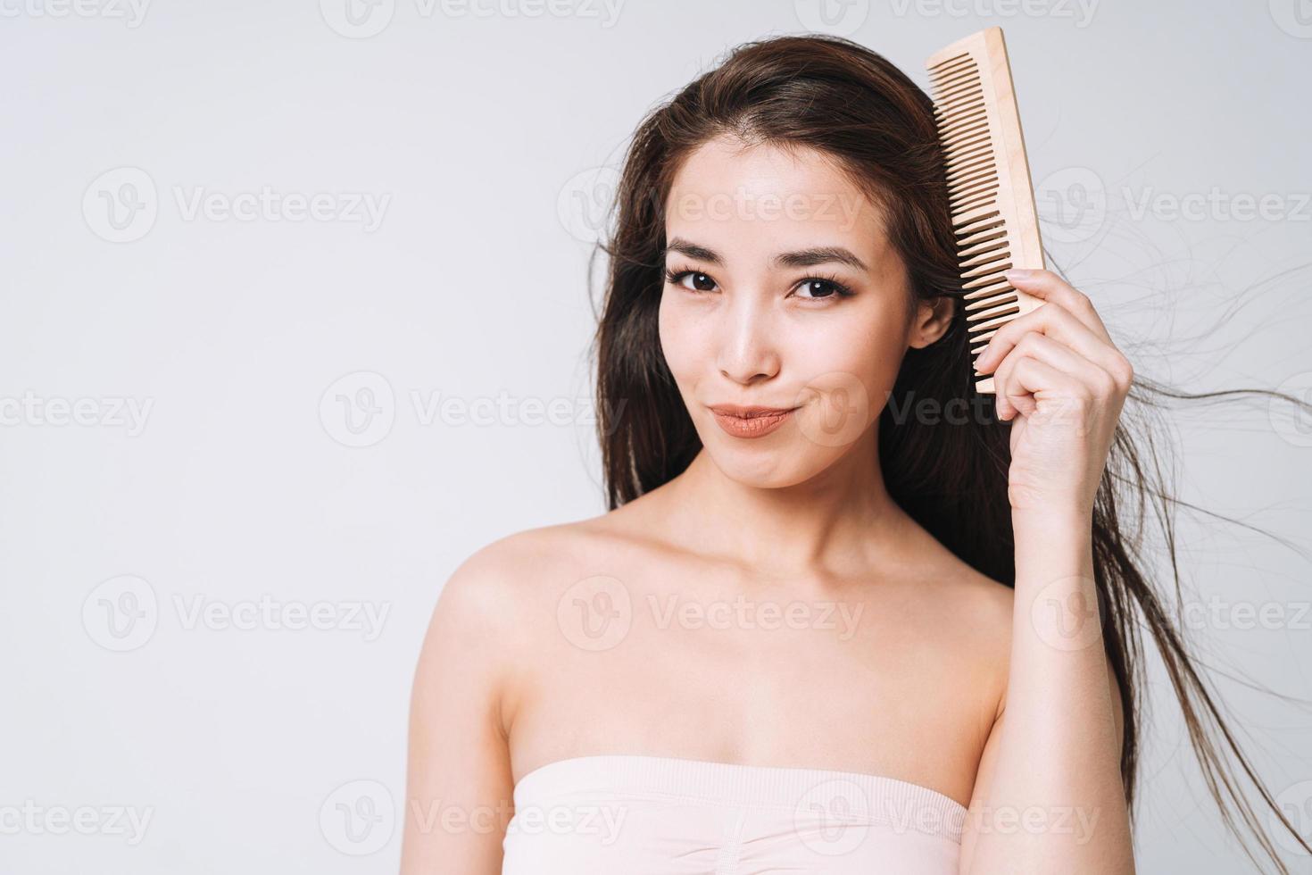 retrato de belleza de mujer asiática sonriente feliz con cabello largo oscuro peinando peine de madera sobre fondo blanco aislado foto