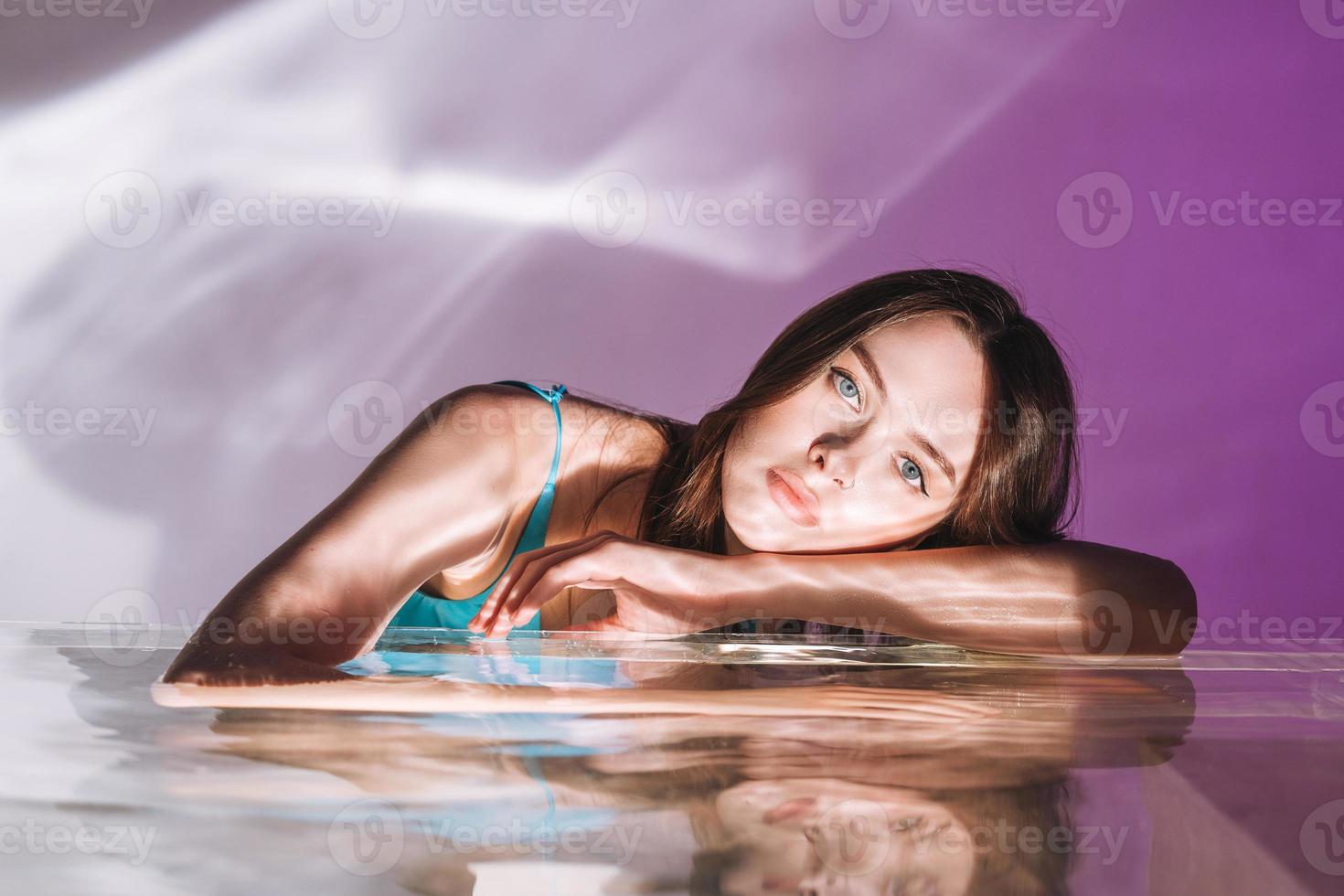 retrato de belleza con agua de una joven modelo de moda con cabello largo oscuro saludable sobre fondo púrpura foto