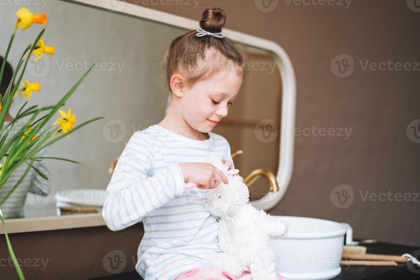 Cute little girl sitting on floor with toy at bright bathroom at home photo