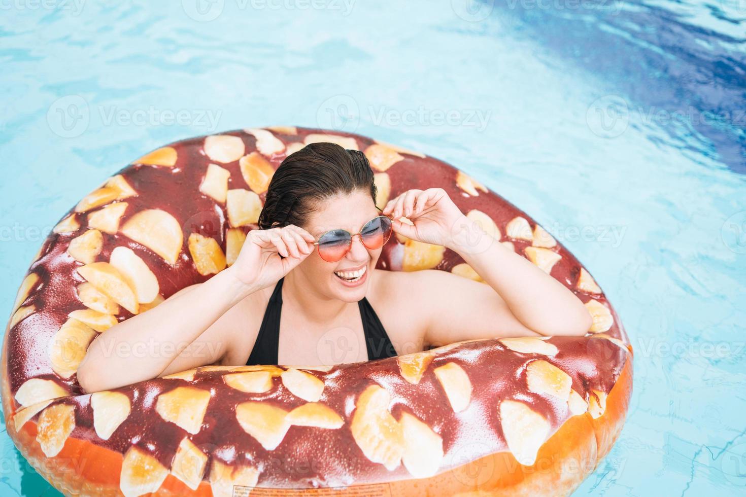 Happy young woman plus size body positive in inflatable doughnut circle swimming in the pool, summer vacations photo