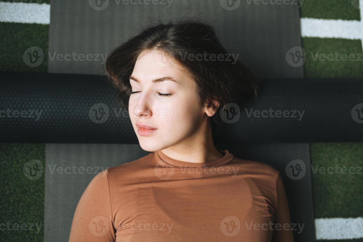 Young brunette woman doing stretching pilates on massage roll in fitness club gym photo