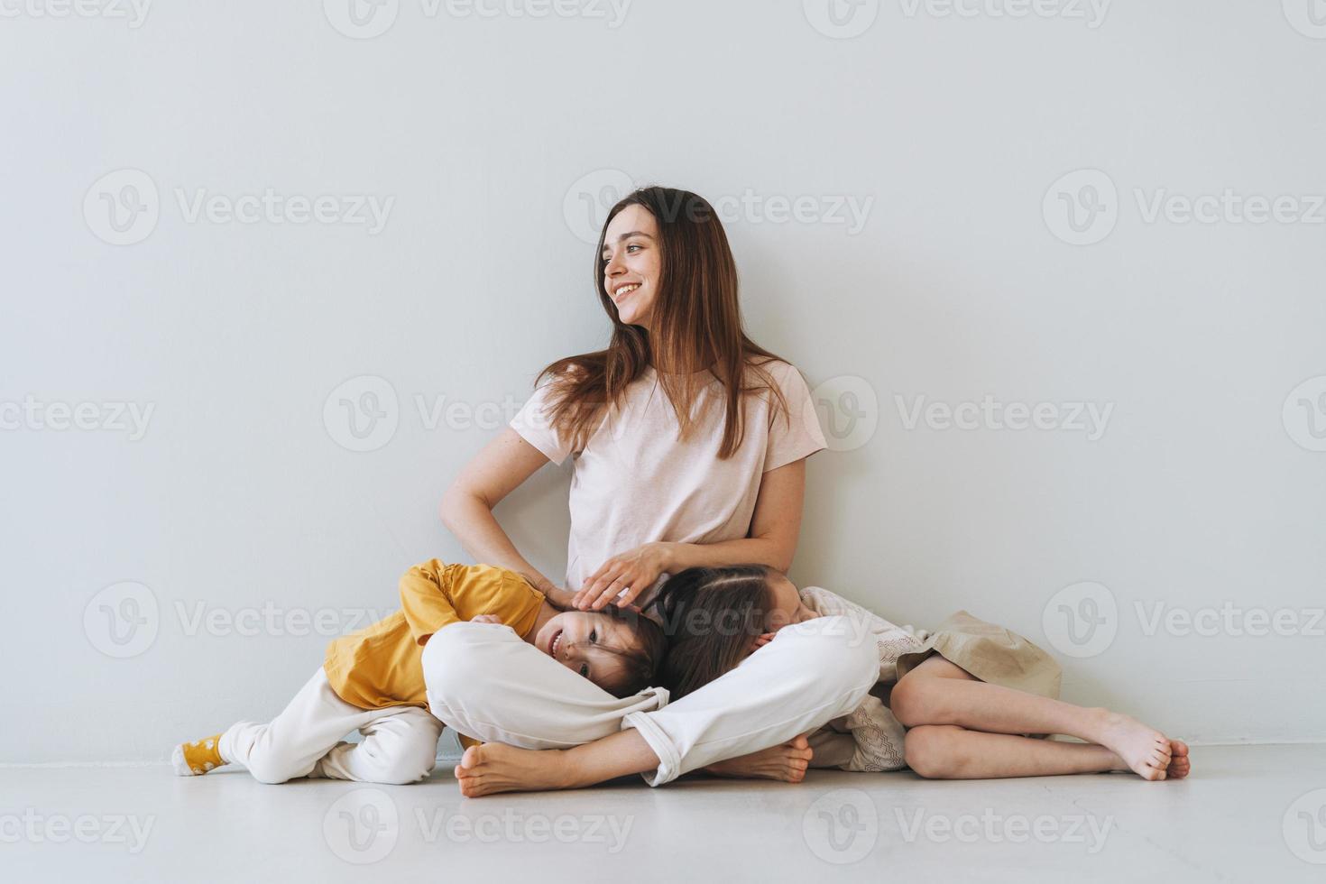 Young happy mother with two children girls on the background of gray wall photo