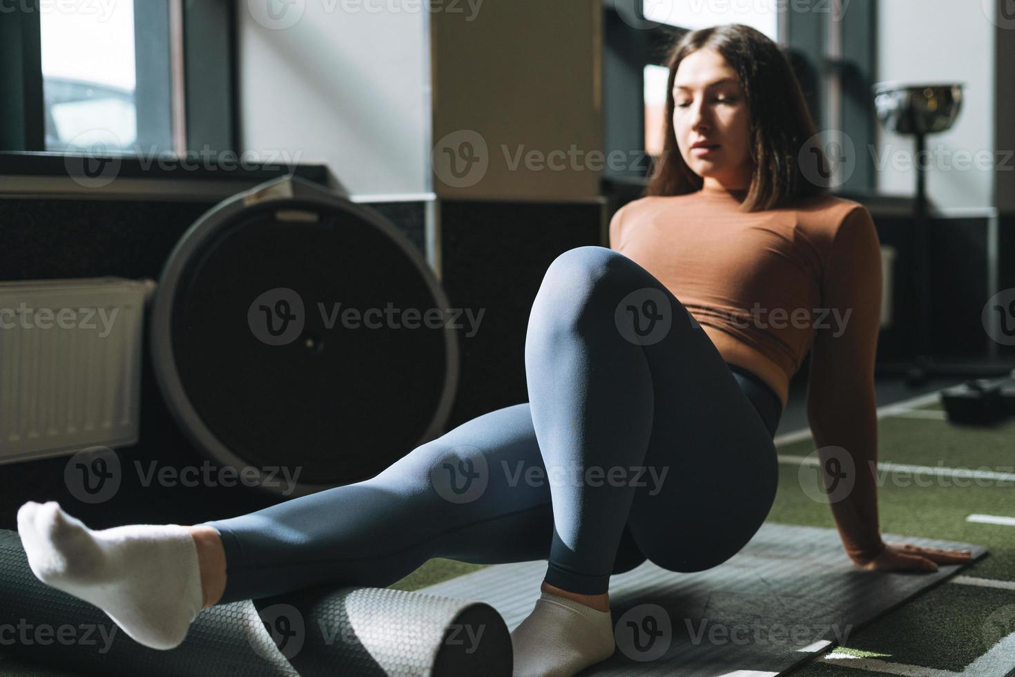 Young brunette woman doing stretching pilates on massage roll in the fitness club gym photo