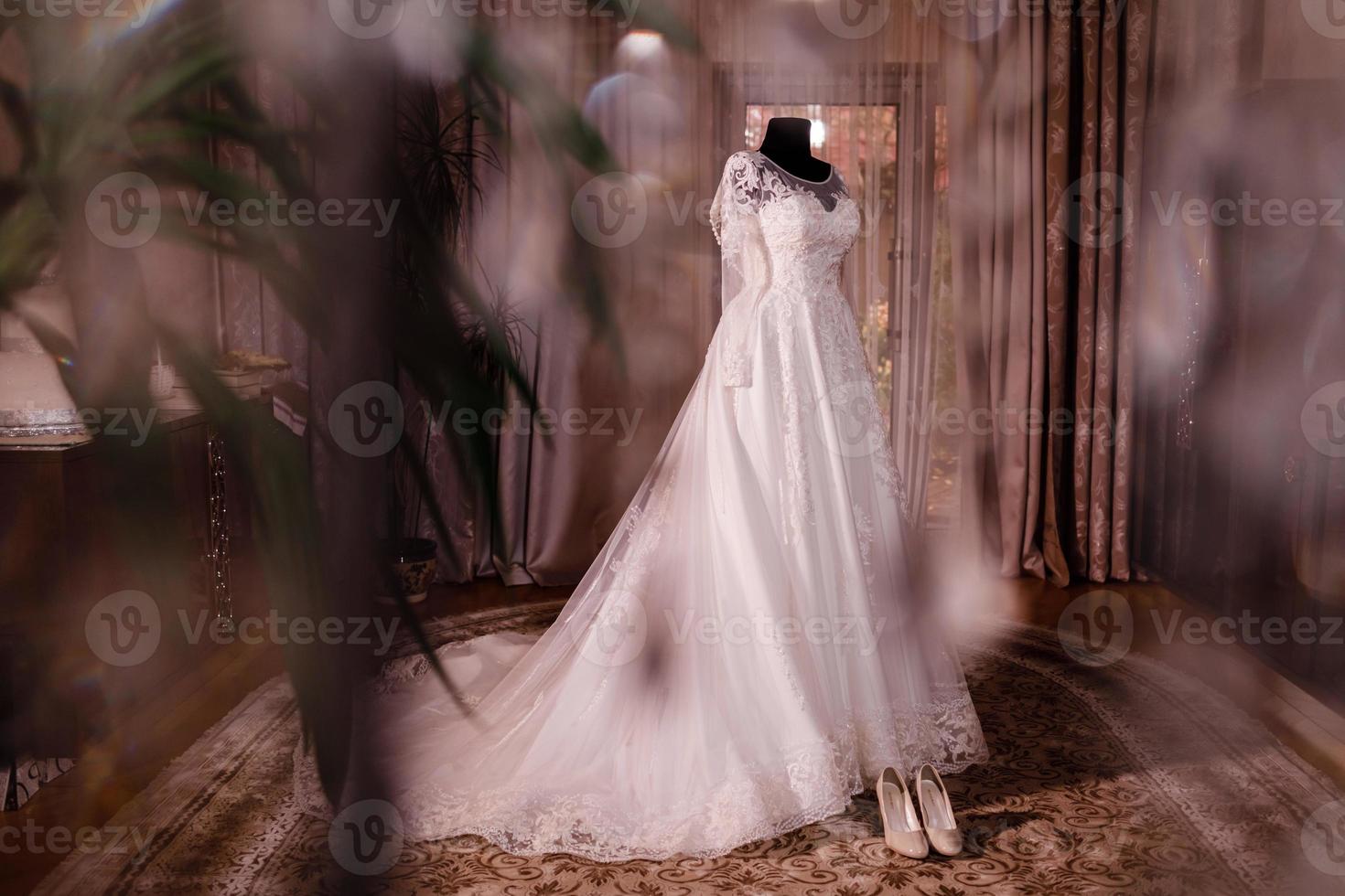 stylish and beautiful wedding dress. classic lace silk wedding dress hanging on hanger in hotel wooden room. morning preparation wedding concept. photo
