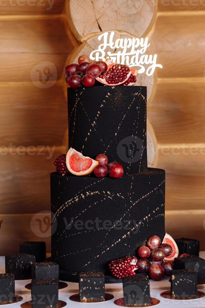 big black birthday cake with fresh fruits and sweets on a festive table. Candy bar. Table with different sweets for party photo