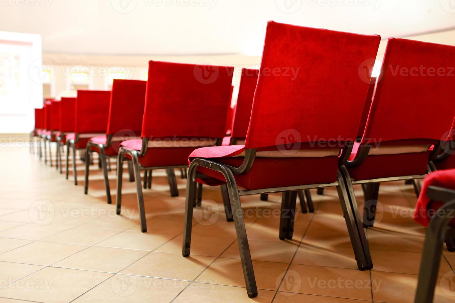 A row of upholstered red textile seats indoors. Chairs for seating the audience at the conference photo