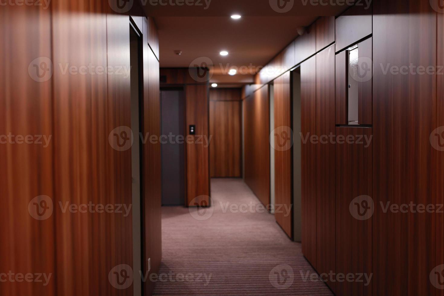 vacío interior oscuro del moderno pasillo del hotel, con paredes revestidas de madera, elegantes alfombras e iluminación en el techo. foto