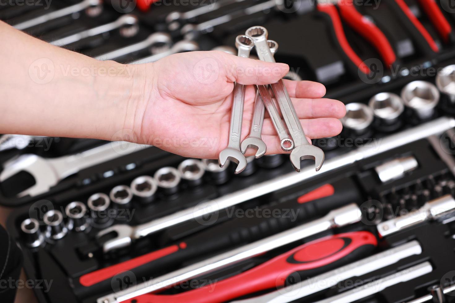 Tool store. Closeup of male hand holding wrenches. Auto repair kit in toolbox. Repairman instruments set. Inside the toolbox there are black-red wrenches, spanners and different nozzles. Closeup. photo