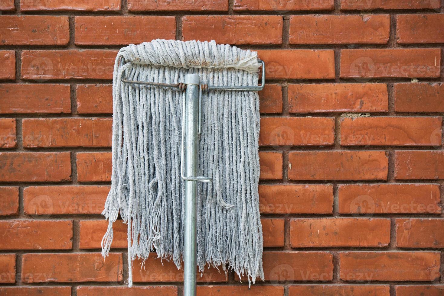 dirty mop against the orange brick wall 1 photo