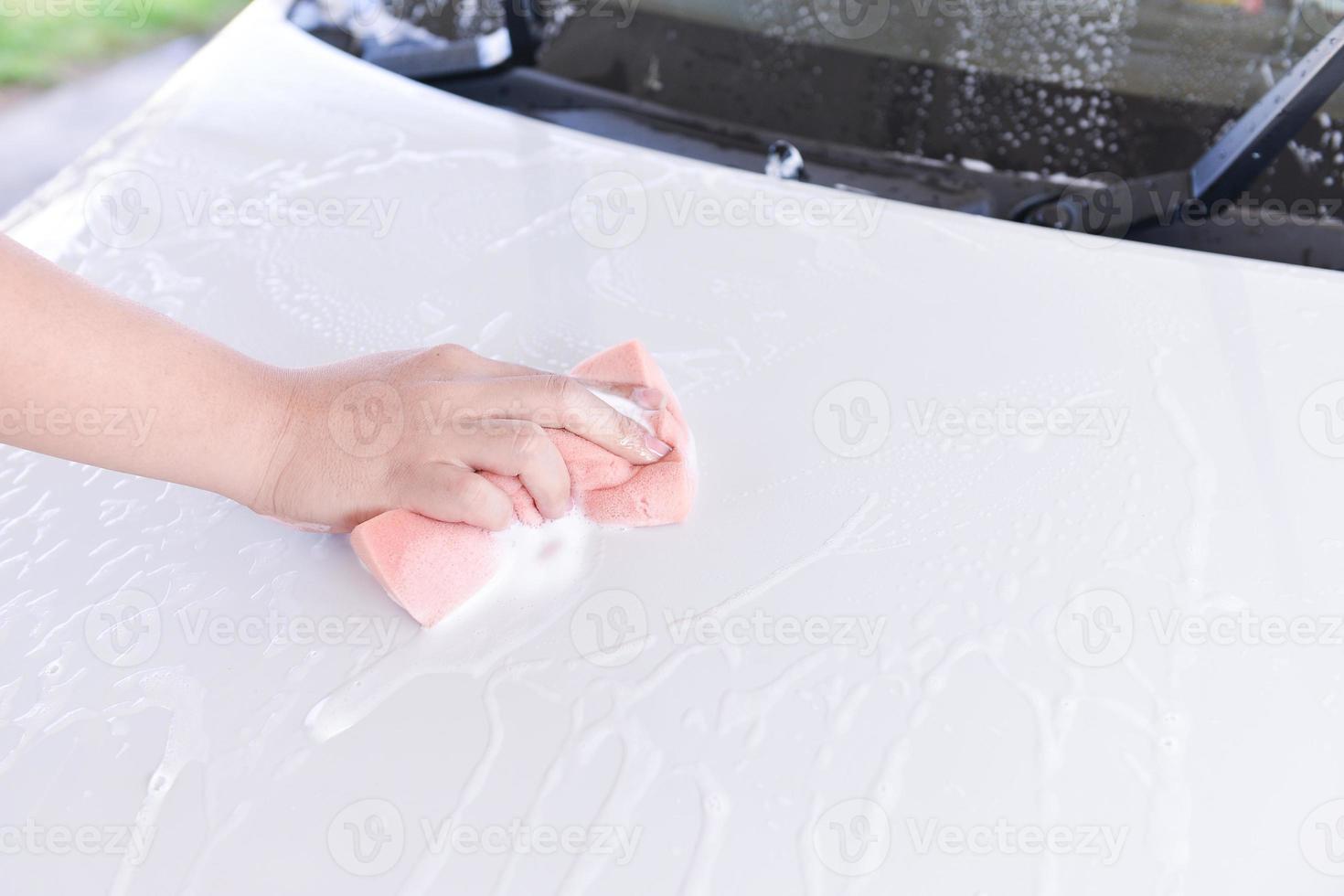 man washing a soapy white car with a pink sponge photo