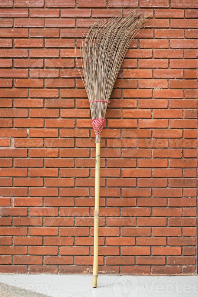 Straw broom against the orange brick wall photo