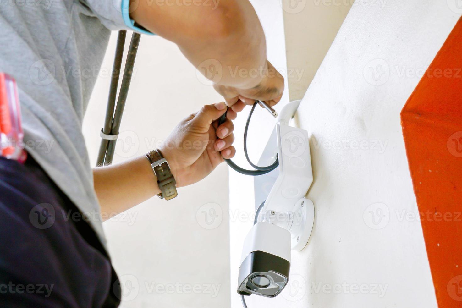 Hands of technician is working connecting power cords to install the CCTV on building wall. photo