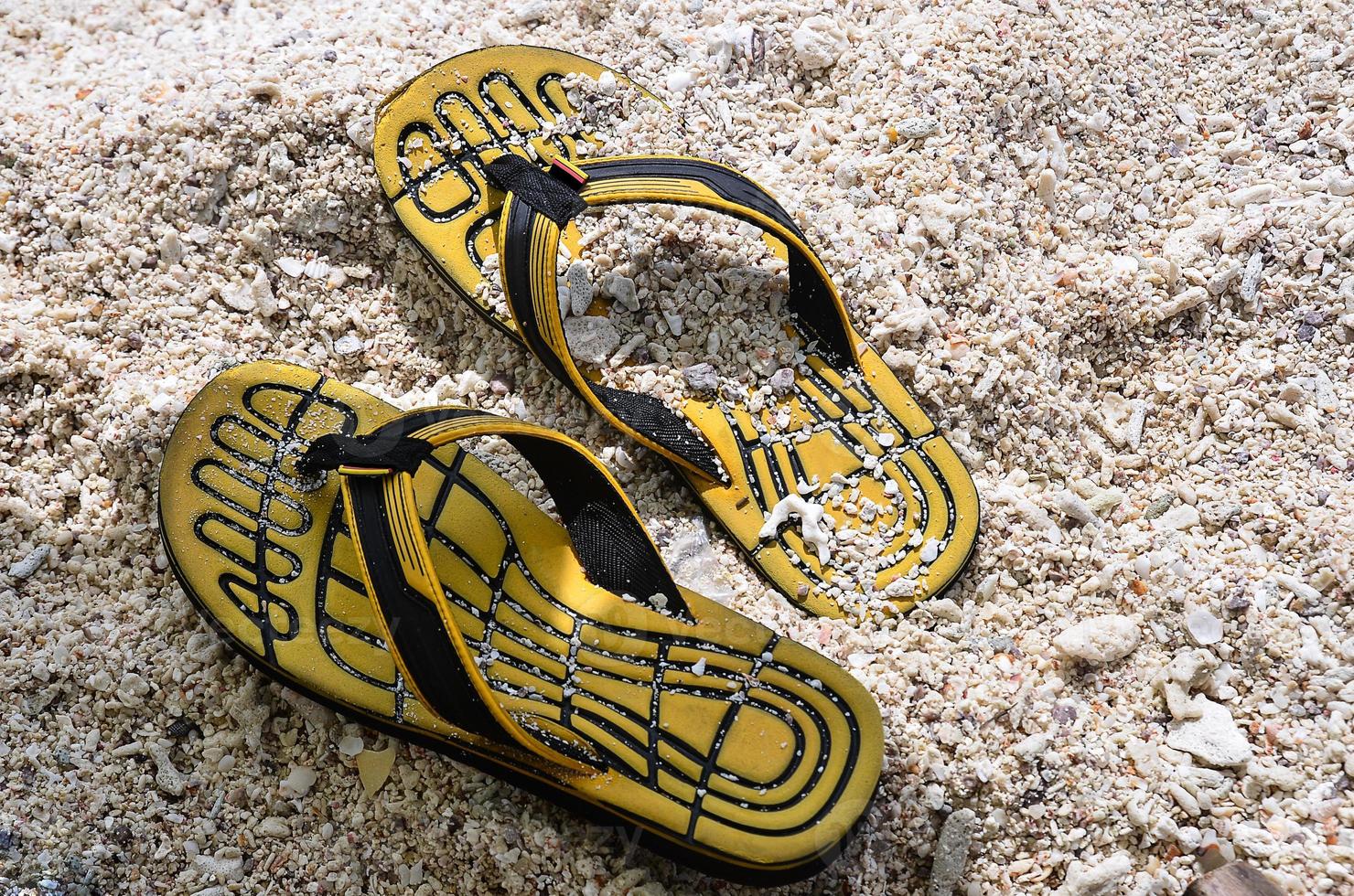 Yellow rubber slippers on sand beach photo