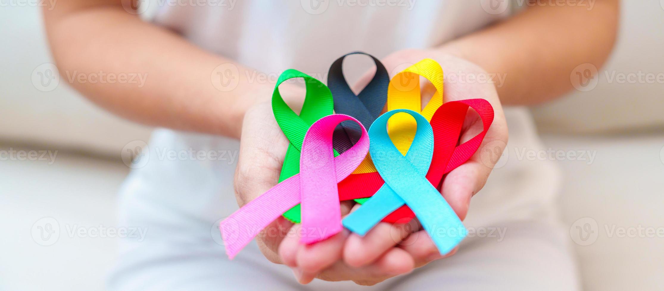 día mundial contra el cáncer, 4 de febrero. mano con cintas azules, rojas, verdes, rosas, negras y amarillas para apoyar a las personas que viven y están enfermas. concepto del día de la concienciación sobre la salud y el autismo foto