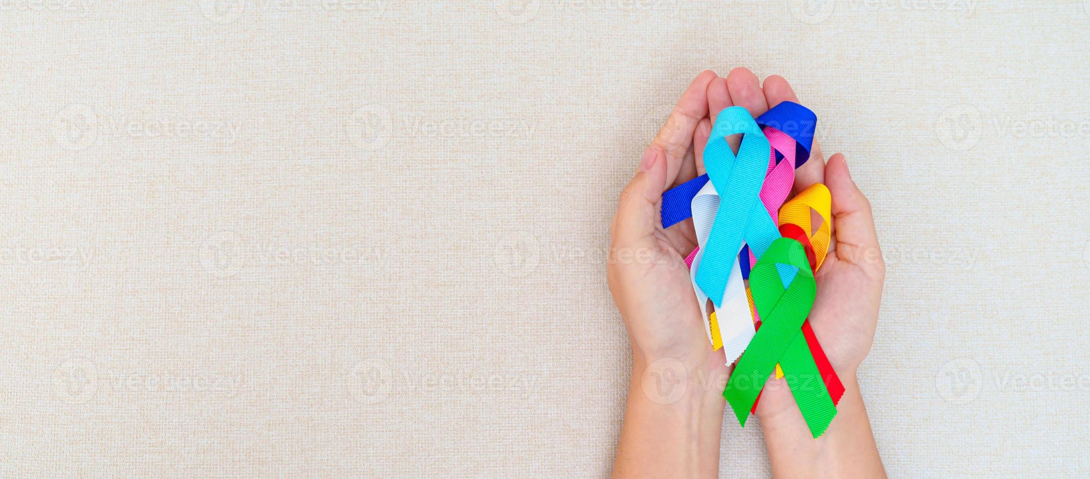 día mundial del cáncer, 4 de febrero. mano con cintas azules, rojas, verdes, blancas, rosas, azul marino y amarillas para apoyar a las personas que viven y están enfermas. concepto del día de la concienciación sobre la salud y el autismo foto