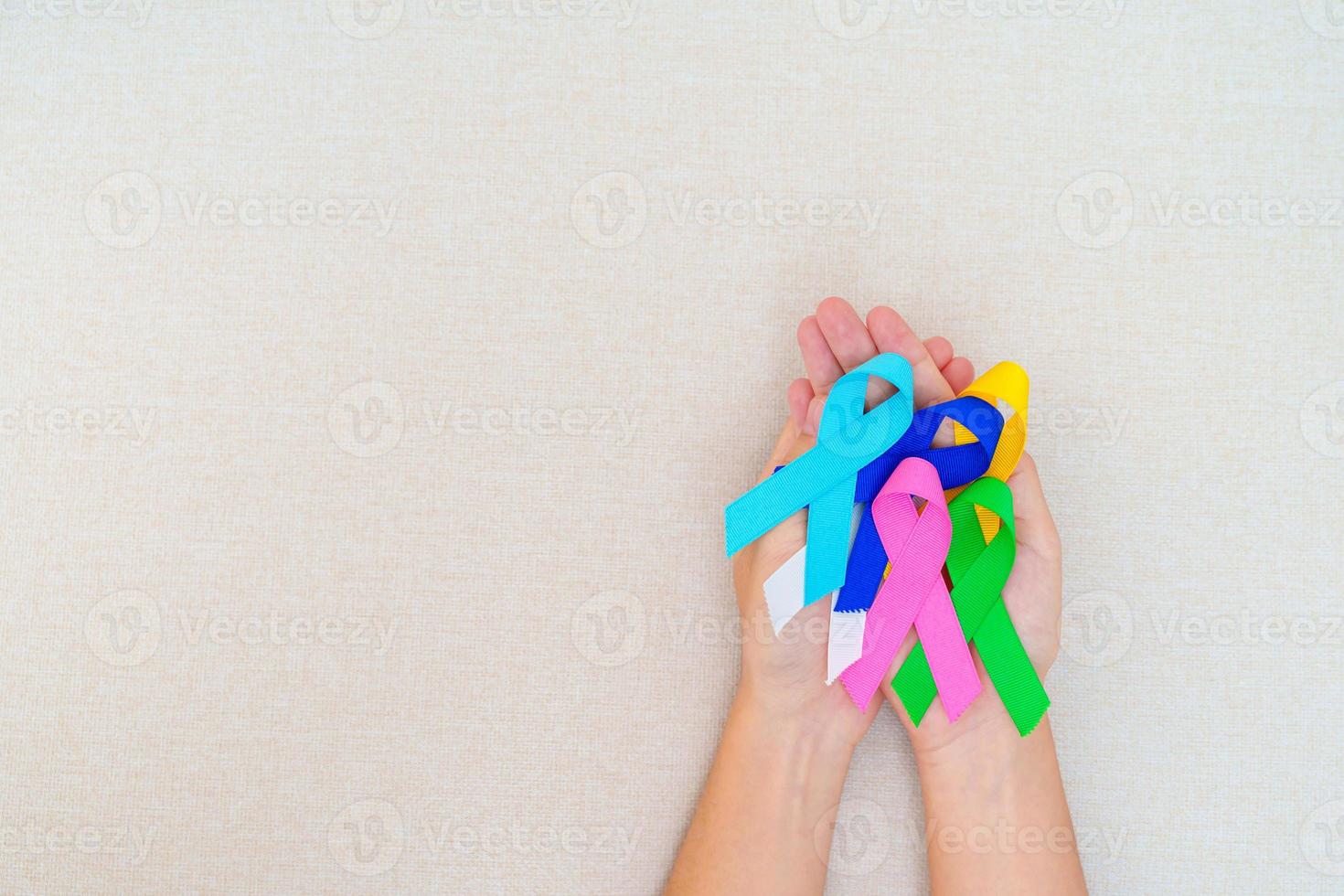 día mundial del cáncer, 4 de febrero. mano con cintas azules, rojas, verdes, blancas, rosas, azul marino y amarillas para apoyar a las personas que viven y están enfermas. concepto del día de la concienciación sobre la salud y el autismo foto