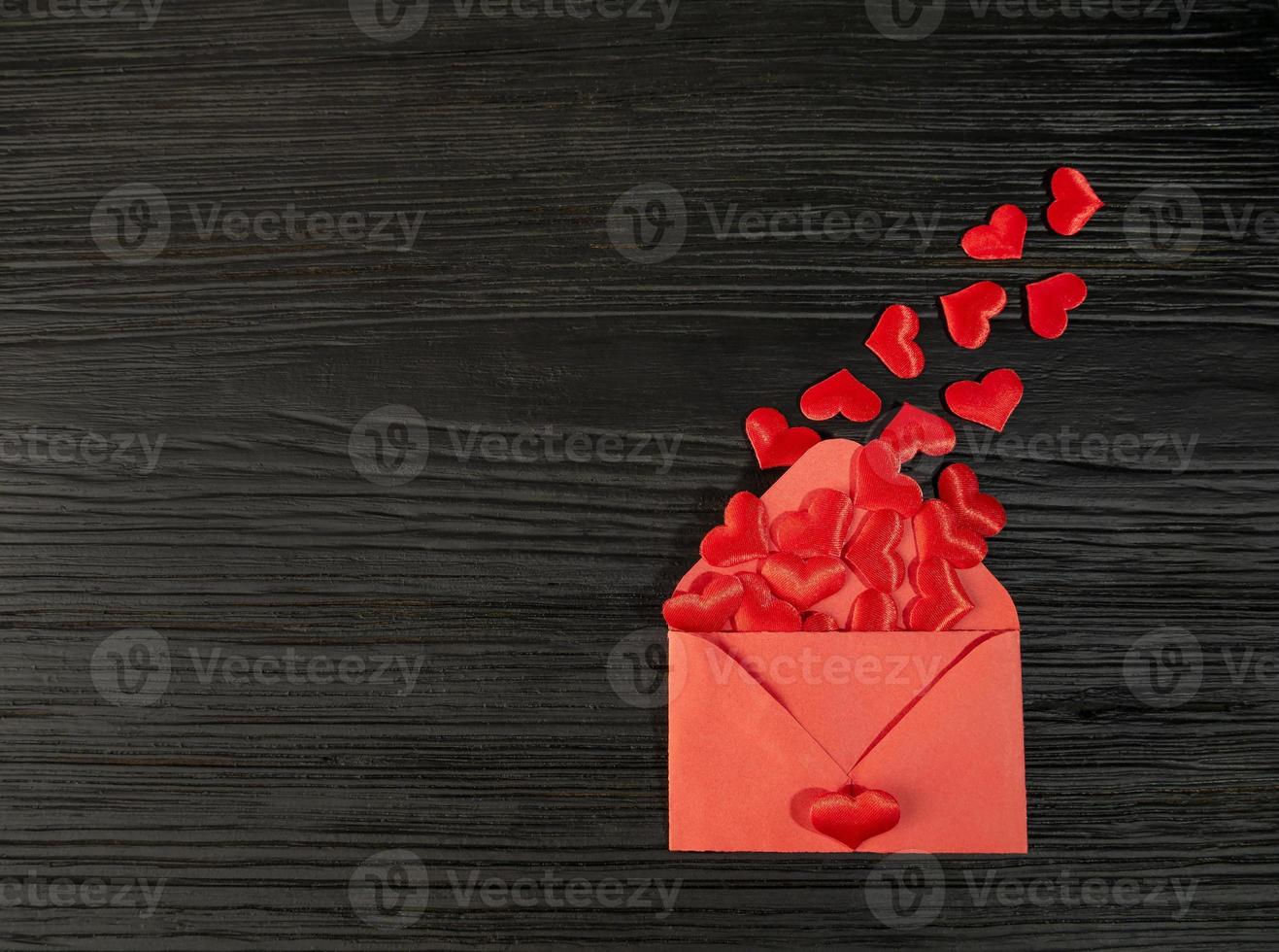 Red envelope with a heart on a black textured wooden background. Sending a message by mail. Valentine's day, birthday, photo